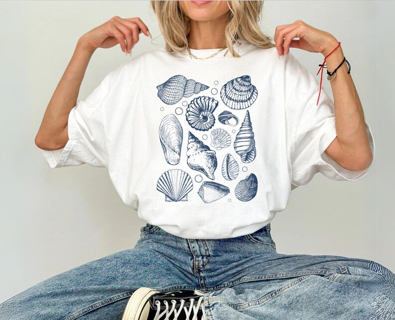 May include: A white t-shirt with a blue and white seashell print. The shirt has a relaxed fit and a crew neck.