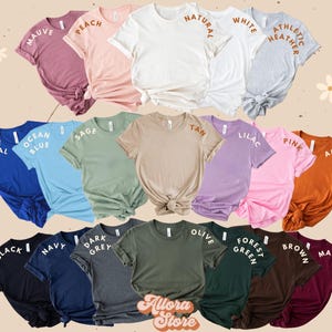 K&ouml;nnte beinhalten: Eine Auswahl an T-Shirts in verschiedenen Farben und Stilen, mit Textlabels, die die Farbnamen angeben. Die Farben umfassen Mauve, Pfirsich, Natur, Wei&szlig;, Athletik-Heather, True Royal, Ozeanblau, Salbei, Braun, Lila, Rosa, Herbst, Schwarz, Marine, Dunkelgrau, Oliv, Waldgr&uuml;n, Braun und Maroon.
