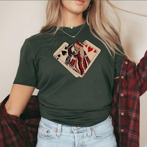 K&ouml;nnte beinhalten: Ein dunkelgr&uuml;nes T-Shirt mit einem Aufdruck von zwei Spielkarten, einer Herzdame und einem Pik-Buben, die sich &uuml;berlappen. Die Dame h&auml;lt eine rote Rose.