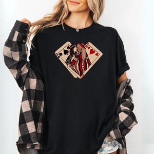 K&ouml;nnte beinhalten: Schwarzes T-Shirt mit einem Aufdruck von zwei Spielkarten, einer Herzdame und einem Pik-Buben, die sich &uuml;berlappen. Die Dame blickt dem Buben entgegen und beide schauen sich an.