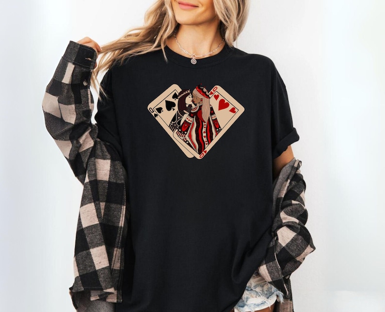 K&ouml;nnte beinhalten: Schwarzes T-Shirt mit einem Aufdruck von zwei Spielkarten, einer Herzdame und einem Pik-Buben, die sich &uuml;berlappen. Die Dame blickt dem Buben entgegen und beide schauen sich an.