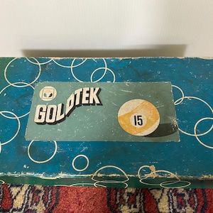 May include: A blue box with a white circle pattern. The box has a label with the text "GOLDTEK" and a white billiard ball with the number "15" on it.