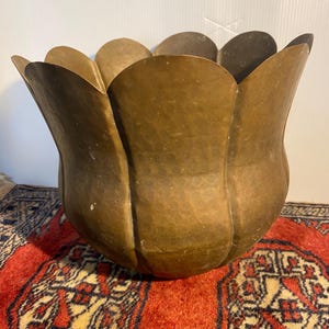 May include: A hammered brass planter with a scalloped, petal-like rim. The vessel features a rounded body with a warm, metallic brown finish and a textured surface created by small, repetitive indentations across the entire exterior of the metal.