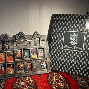 May include: A silver-toned metal schoolhouse-shaped multi-photo frame with twelve individual picture slots, each labelled with grade levels from kindergarten through twelfth grade, alongside its original black and white patterned box.
