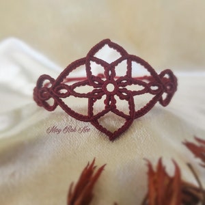 Può includere: Un braccialetto all'uncinetto color granata con un design a fiore. Il braccialetto è realizzato con un motivo delicato e intricato.