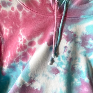 Details of a tie dye baby blue and baby pink hoodie. Close up image of hood straps and hoodie stiches. Hoodie made from soft organic cotton material.