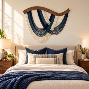 May include: A wall hanging featuring a curved dark wood top piece with multiple draped strands of rope in shades of cream, light blue, and dark navy blue. The rope strands are arranged in overlapping, cascading U-shaped patterns.