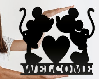 Puede incluir: Silueta de metal negro de Mickey Mouse y Minnie Mouse sosteniendo un corazón con la palabra "WELCOME" debajo.
