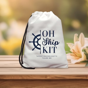 May include: A white drawstring bag with a navy blue nautical design and the words "OH Ship KIT". The bag features a ship's wheel graphic and the text "Tatum's Bachelorette Tulum, MX". The bag is on a wooden surface.