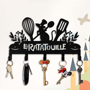 May include: Black metal key holder with a silhouette of a rat chef holding a spoon and a whisk. The holder has six hooks and the text "La Ratatouille" is written on the front.
