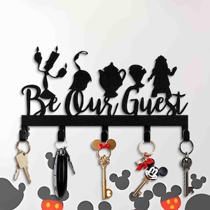 May include: Black metal key holder with the phrase "Be Our Guest" and silhouettes of characters. The key holder has five hooks with keys and keychains attached, including a Mickey Mouse key.