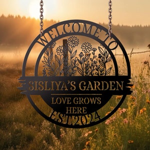 May include: Black metal welcome sign with a floral design, the text "Welcome to Sisliya's Garden Love Grows Here Est 2024" and a chain for hanging.