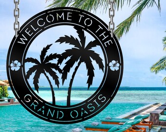 Könnte beinhalten: Schwarzes Metallschild mit dem Text "Willkommen im Grand Oasis" in einem weißen Kreis mit Palmen und Hibiskusblüten.