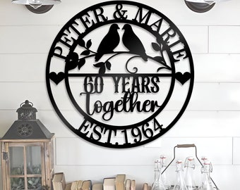 Könnte beinhalten: Schwarzes Metallschild mit dem Text "Peter & Marie 60 Years Together Est. 1964" und zwei Vögeln, die auf einem Zweig mit Blättern sitzen. Das Schild ist rund und hat auf jeder Seite eine Herzform.