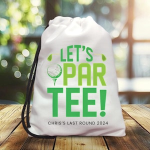 Puede incluir: Bolsa blanca con cordón con el texto "LET'S PAR TEE!" en verde, junto con un gráfico de pelota de golf. El texto "CHRIS'S LAST ROUND 2024" está impreso debajo. La bolsa tiene cordones negros.