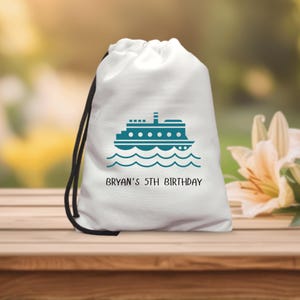 Puede incluir: Bolsa blanca con cordón y una ilustración turquesa de un ferry sobre olas. El texto "BRYAN'S 5TH BIRTHDAY" está impreso debajo. La bolsa tiene cordones negros y está sobre una superficie de madera.