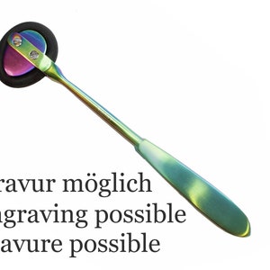Könnte beinhalten: Ein Reflexhammer mit einem regenbogenfarbenen Metallgriff und Kopf. Der Kopf hat einen schwarzen Gummiring um einen metallischen Mittelteil. Der Text "Gravur möglich engraving possible gravure possible" ist unter dem Hammer aufgedruckt.