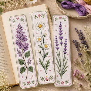 May include: Three rectangular fabric bookmarks featuring detailed cross-stitch embroidery of floral designs. The left bookmark displays purple lilac flowers, the center shows white daisies, and the right features purple lavender stalks on white fabric.