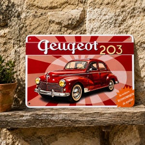 Op de afbeelding: Een rechthoekig metalen bord met een rood-witte zonnestraal-achtergrond en een illustratie van een vintage rode Peugeot 203 auto. De tekst bovenaan luidt Peugeot 203 en onderaan staat la voiture ÉCONOMIQUE de qualité.