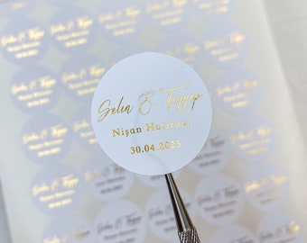 以下が含まれることがあります： 金色の文字が書かれた白い丸いステッカーのシート。ステッカーには「Gelin & Damat Nisan Havasi 30.04.2023」と書いてあります。