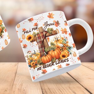 May include: White ceramic mug with a fall-themed design featuring a wooden cross with a plaid scarf, pumpkins, sunflowers, and leaves. The text "Fall for Jesus He Never Leaves" is printed on the mug.