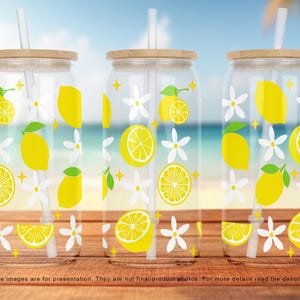 May include: Three clear glass tumblers with wooden lids and straws. Each tumbler has a lemon and white flower design.
