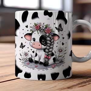 May include: White ceramic mug with a black and white cartoon cow wearing a flower crown. The cow is sitting in a field of flowers and butterflies. The mug has a black and white cow print design.
