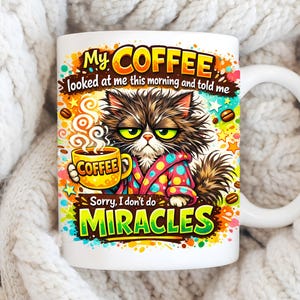 May include: White ceramic coffee mug featuring a grumpy cat illustration. The cat is wearing a robe and holding a coffee cup. Text on the mug reads "My Coffee looked at me this morning and told me...Sorry, I don't do MIRACLES."