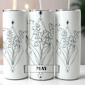 May include: Three white stainless steel tumblers with a black and white geometric design featuring a lily of the valley flower. The middle tumbler has the word "MAY" printed on a banner.