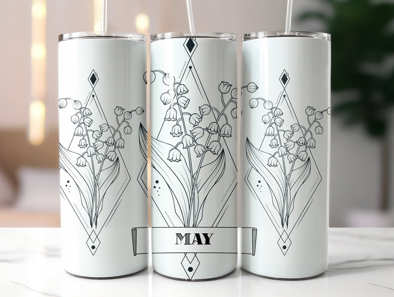 May include: Three white stainless steel tumblers with a black and white geometric design featuring a lily of the valley flower. The middle tumbler has the word "MAY" printed on a banner.