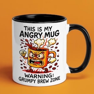 Puede incluir: Taza de cerámica blanca con interior y asa negros. La taza presenta una ilustración de dibujos animados de una taza de café enfadada con el texto "THIS IS MY ANGRY MUG" y "WARNING: GRUMPY BREW ZONE".