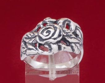 Könnte beinhalten: Ein silberner Ring mit einem detaillierten Rosenmotiv. Die Rose ist mittig auf dem Ring platziert und hat ein Spiralmuster in der Mitte. Der Ring befindet sich auf einem durchsichtigen Ständer.