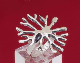 Puede incluir: Un anillo de plata con un diseño de árbol. El anillo está en un expositor transparente.