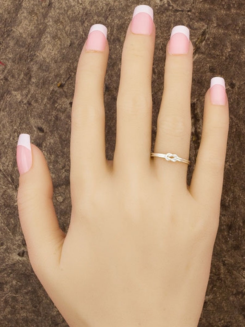 May include: A gold knot ring on a hand with white-tipped fingernails.