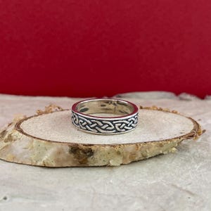 Puede incluir: Un anillo de plata con un diseño de nudo celta. El anillo está sobre una superficie de madera.
