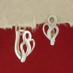 Puede incluir: Un par de pendientes de plata con un diseño único y abstracto. Los pendientes tienen forma de una serie de bucles entrelazados.