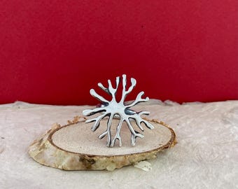 Puede incluir: Un anillo de plata con un diseño de árbol. El anillo está sobre un pequeño disco de madera.