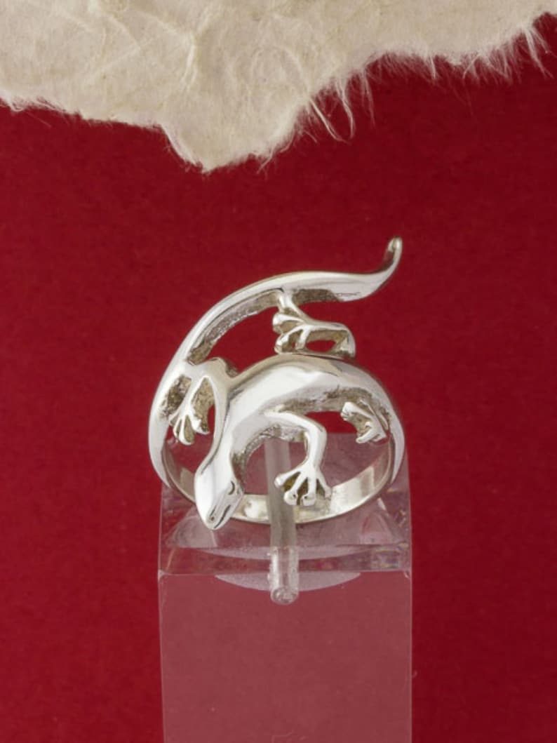 K&ouml;nnte beinhalten: Ein silberner Ring mit einem detaillierten, dreidimensionalen Design einer Eidechse. Die Eidechse ist um den Ringband gewickelt, wobei ihr Schwanz um die Oberseite des Rings gewickelt ist.