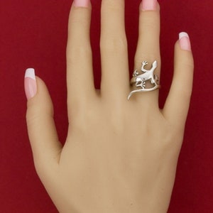 K&ouml;nnte beinhalten: Ein silberner Ring mit einem Eidechsen-Design. Der Ring wird am Mittelfinger einer Hand mit wei&szlig;en French Manik&uuml;re-N&auml;geln getragen.