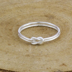 May include: A silver knot ring with a simple design. The ring is made of two bands of metal that are twisted together to form a knot.