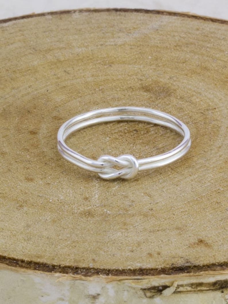 May include: A silver knot ring with a simple design. The ring is made of two bands of metal that are twisted together to form a knot.