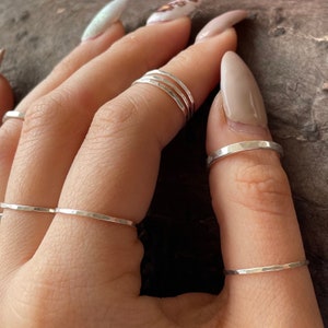 May include: A hand wearing multiple thin silver rings on different fingers. The rings are hammered and have a textured finish.