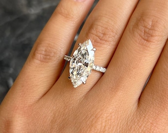 May include: A marquise cut diamond engagement ring with a pave setting. The ring is set in white gold and features a large, sparkling diamond.