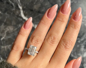 Könnte beinhalten: Nahaufnahme einer Hand, die einen silbernen Ring mit einem großen, rechteckigen Diamanten im Smaragdschliff trägt. Die Hand hat eine hellrosa Maniküre mit mandelförmigen Nägeln.