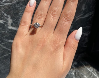 May include: A hand with white almond-shaped nails is wearing a silver ring with a large, round, clear diamond.