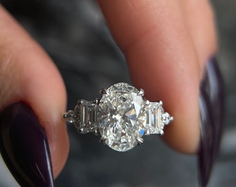 Könnte beinhalten: Ein silberner Ring mit einem großen ovalen Diamanten und zwei kleineren Baguette-förmigen Diamanten auf jeder Seite.
