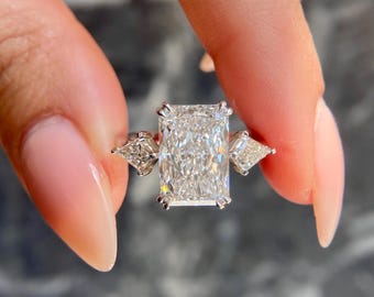 Könnte beinhalten: Ein silberner Ring mit einem großen, rechteckigen, klaren Diamanten in der Mitte. Zwei kleinere, dreieckige, klare Diamanten befinden sich auf beiden Seiten des mittleren Diamanten.