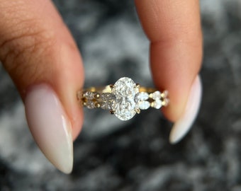 May include: A gold engagement ring with a large oval-shaped diamond and smaller diamonds set in a pave setting.