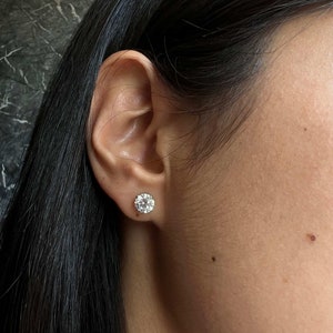 May include: A close-up of a person's ear with a small, round, clear diamond stud earring.