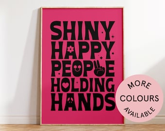 May include: Pink poster with black text that reads "Shiny Happy People Holding Hands". The text is in a retro font style with various graphic elements. A pink circle with black text reads "More Colours Available".